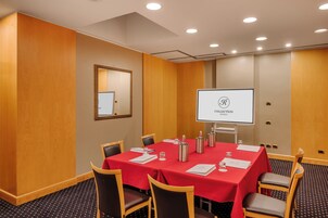A conference room with a red table, chairs, a projector screen, and a wooden panel wall.