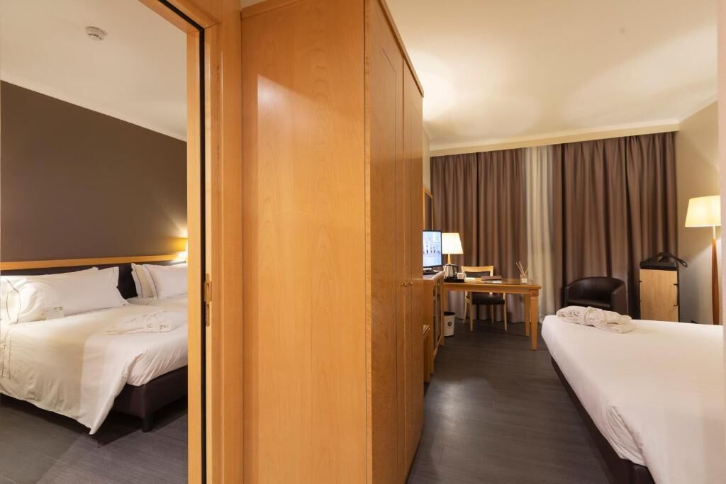 Habitación de hotel con dos camas, un escritorio, una silla y una lámpara.