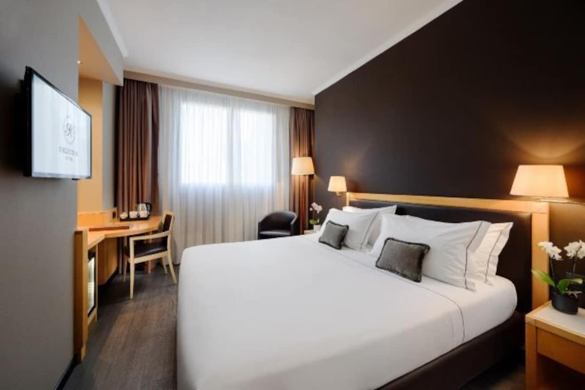 Habitación de hotel con una cama grande, un escritorio, una silla, un televisor y una ventana con cortinas.