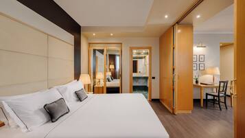Habitación de hotel con una cama grande, un escritorio con silla y un baño visible a través de una puerta abierta.