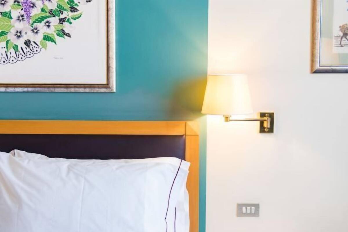 Ein Hotelzimmer mit einem Bett, einer Wandlampe und einem gerahmten Blumenbild.