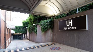 Entrada do Jet Hotel com galeria coberta, placa de identificação e portão.