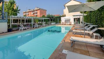 A swimming pool with lounge chairs and umbrellas, surrounded by buildings and greenery.