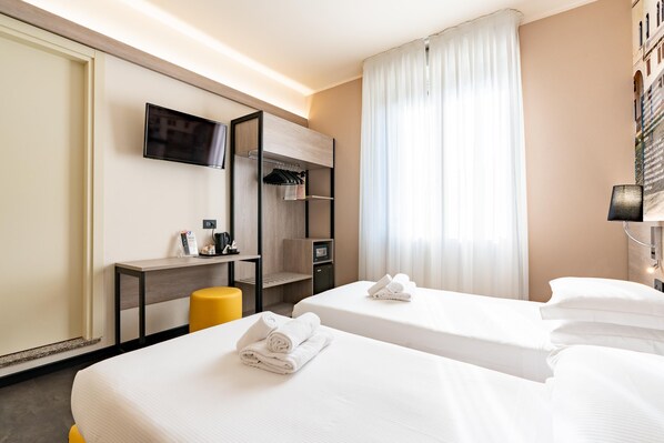 A hotel room with two beds, a TV mounted on the wall, a desk with a chair, and a window with curtains.