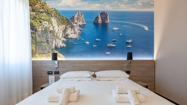 Quarto de hotel com uma cama grande, duas almofadas brancas e toalhas bem dobradas.