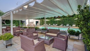 Uma área de estar coberta ao ar livre, com móveis de vime e uma piscina ao fundo.