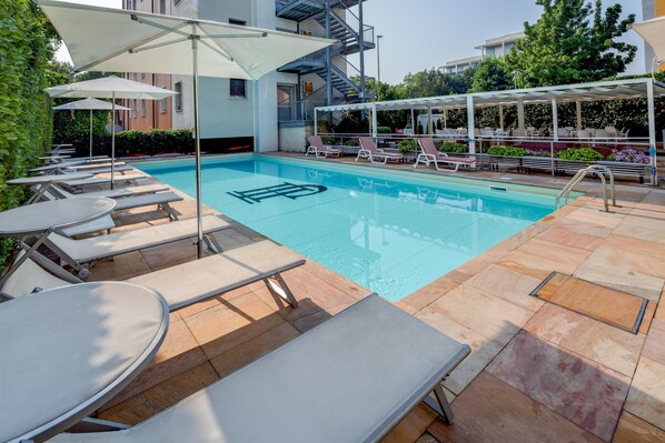 A swimming pool with lounge chairs and umbrellas, surrounded by a tiled deck.