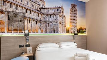 A hotel room with a large bed, a desk with a phone and a lamp, and a mural of the Leaning Tower of Pisa.