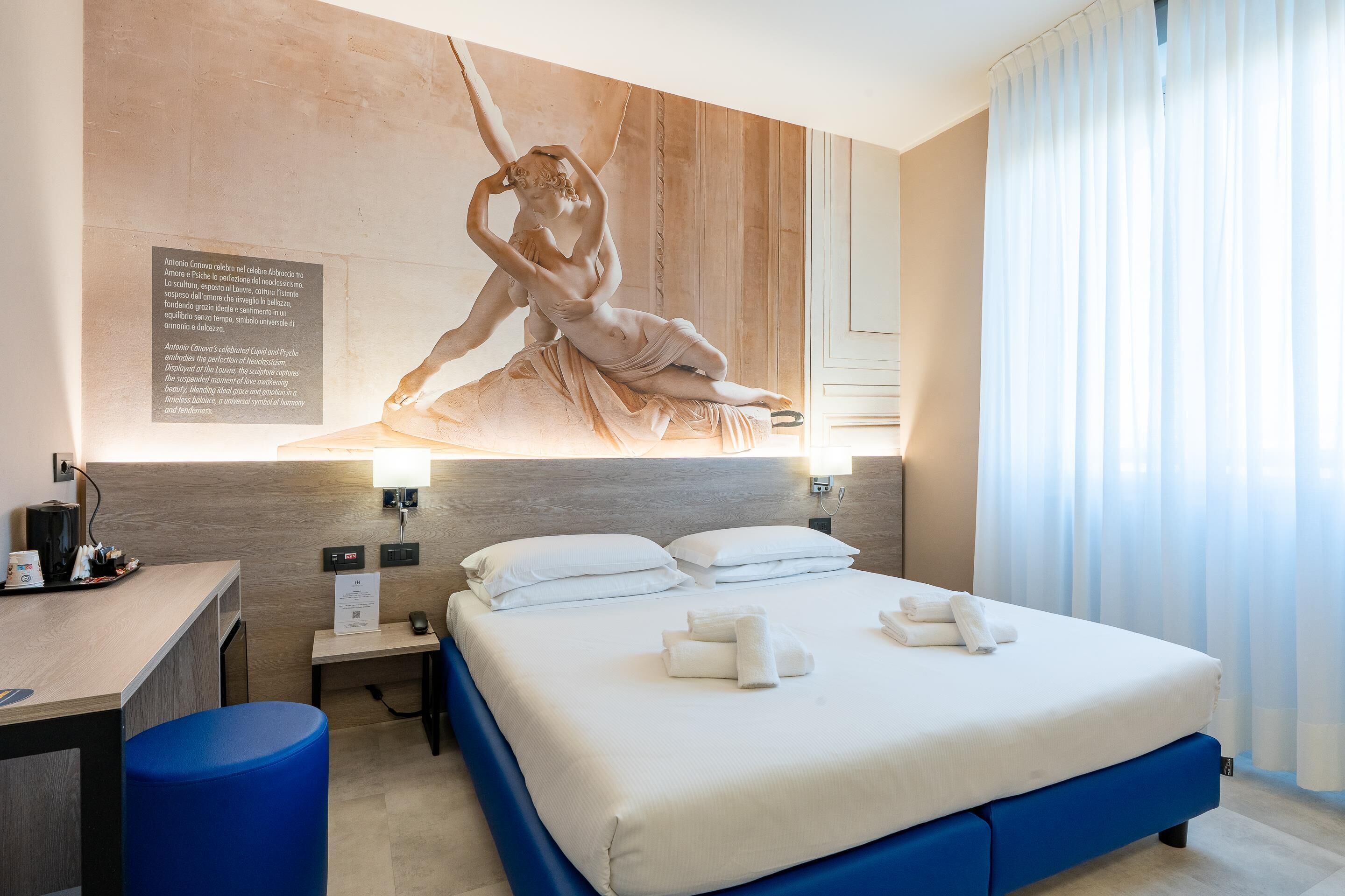 Una camera d'albergo con un letto, una scrivania, una sedia e una scultura a parete.