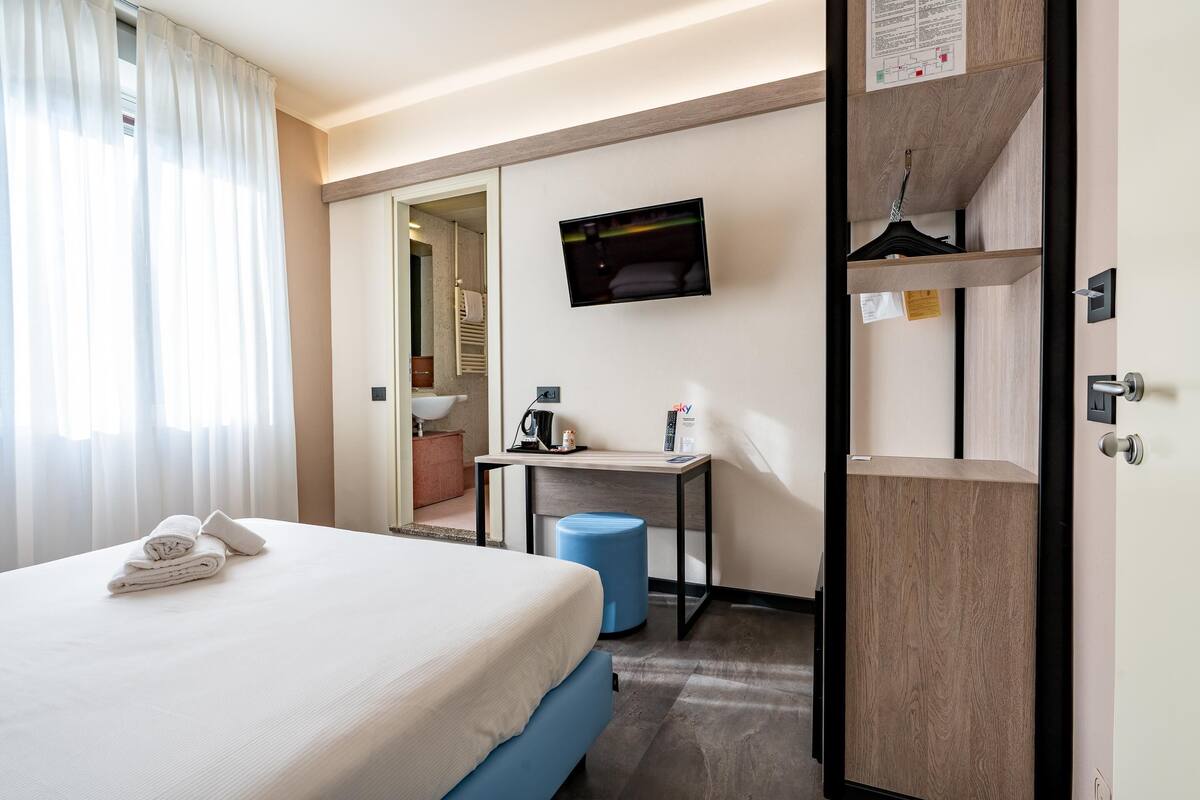 A hotel room with a bed, a desk, a TV, and a wardrobe.