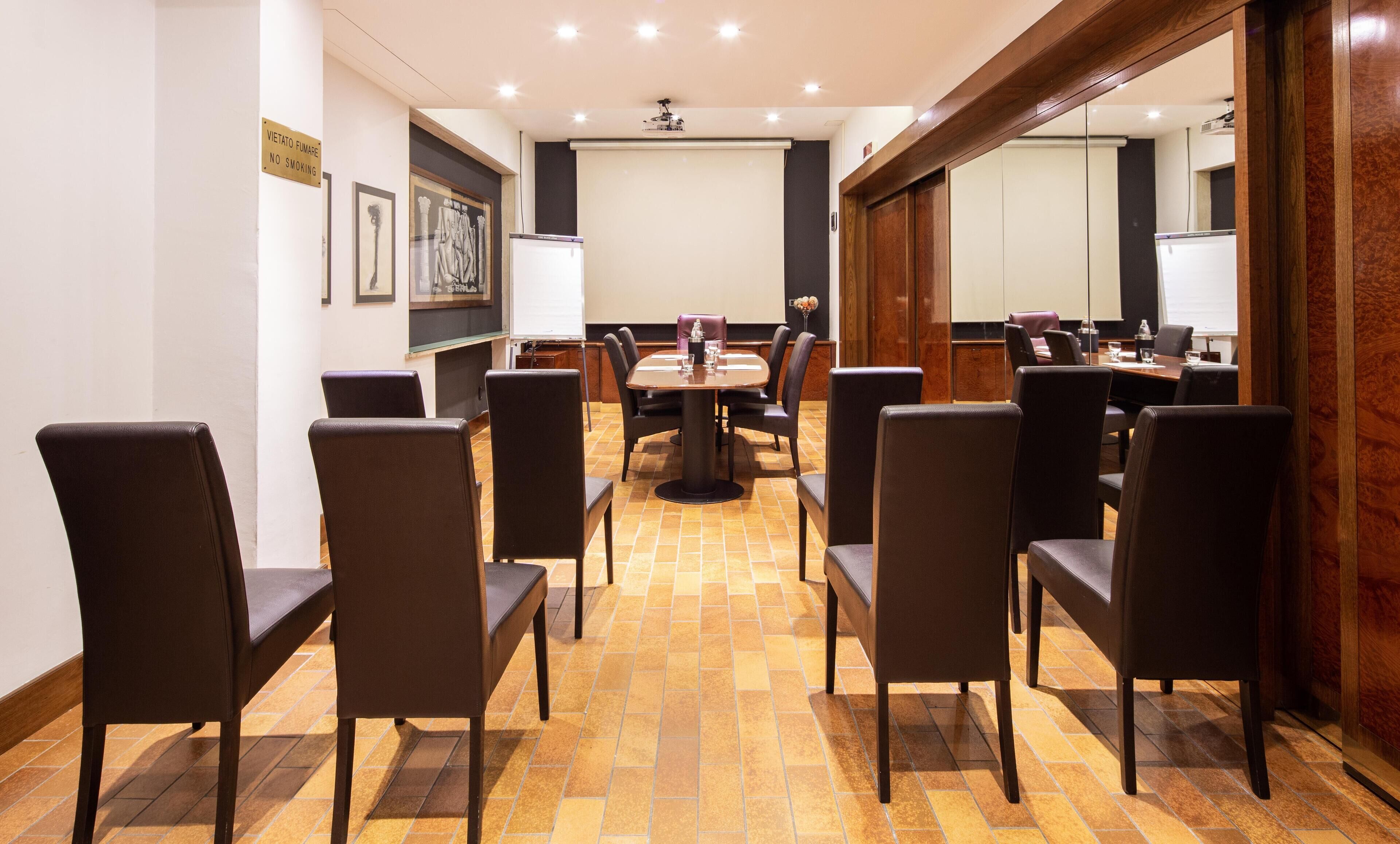 A conference room with a large table and chairs, a projector screen, and framed artwork on the walls.