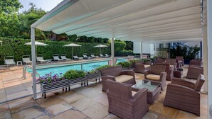 Uma área externa coberta com piscina, espreguiçadeiras e mobiliário de vime.