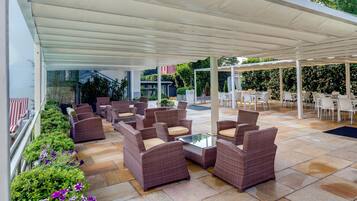 An outdoor patio area with wicker furniture and a glass table, surrounded by stone tiles and covered by a white canopy.