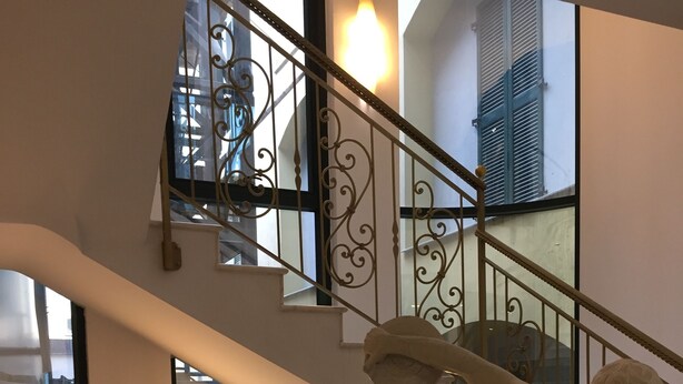 A marble statue of a figure on a pedestal in a lobby with a staircase and glass doors.