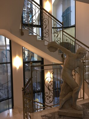 A marble statue of a figure on a pedestal in a lobby with a staircase and glass doors. - Marconi Hotel (Milan)