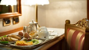 A breakfast tray with eggs, toast, fruit, and a teapot on a table in a room with a mirror and lamps.