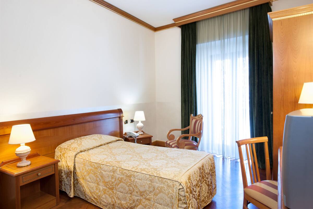 A hotel room with a bed, a chair, a desk with a lamp, and a television.