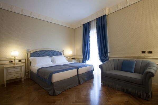 Un dormitorio con cama doble, mesita de noche, lámpara, sofá y ventana con cortinas.
