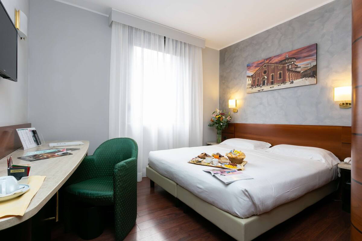 Een hotelkamer met een bed, een bureau met stoel, een flatscreen televisie en een schilderij aan de muur.