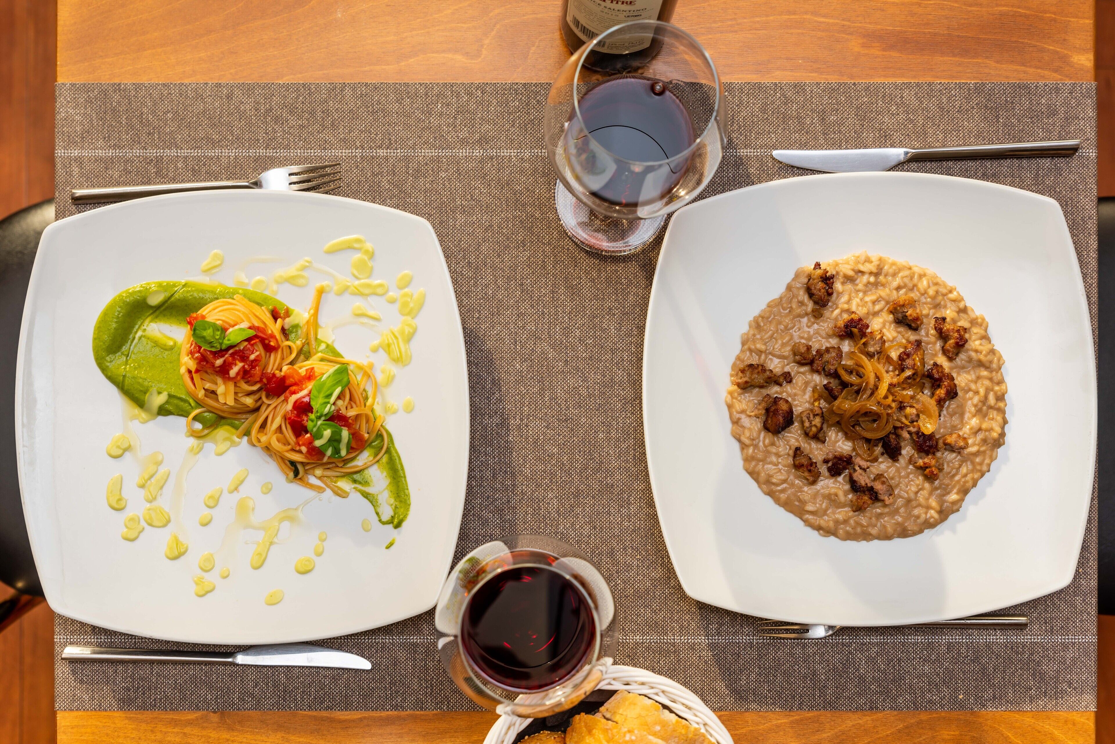 Two plates of food on a table with a wine glass and a bottle of wine.