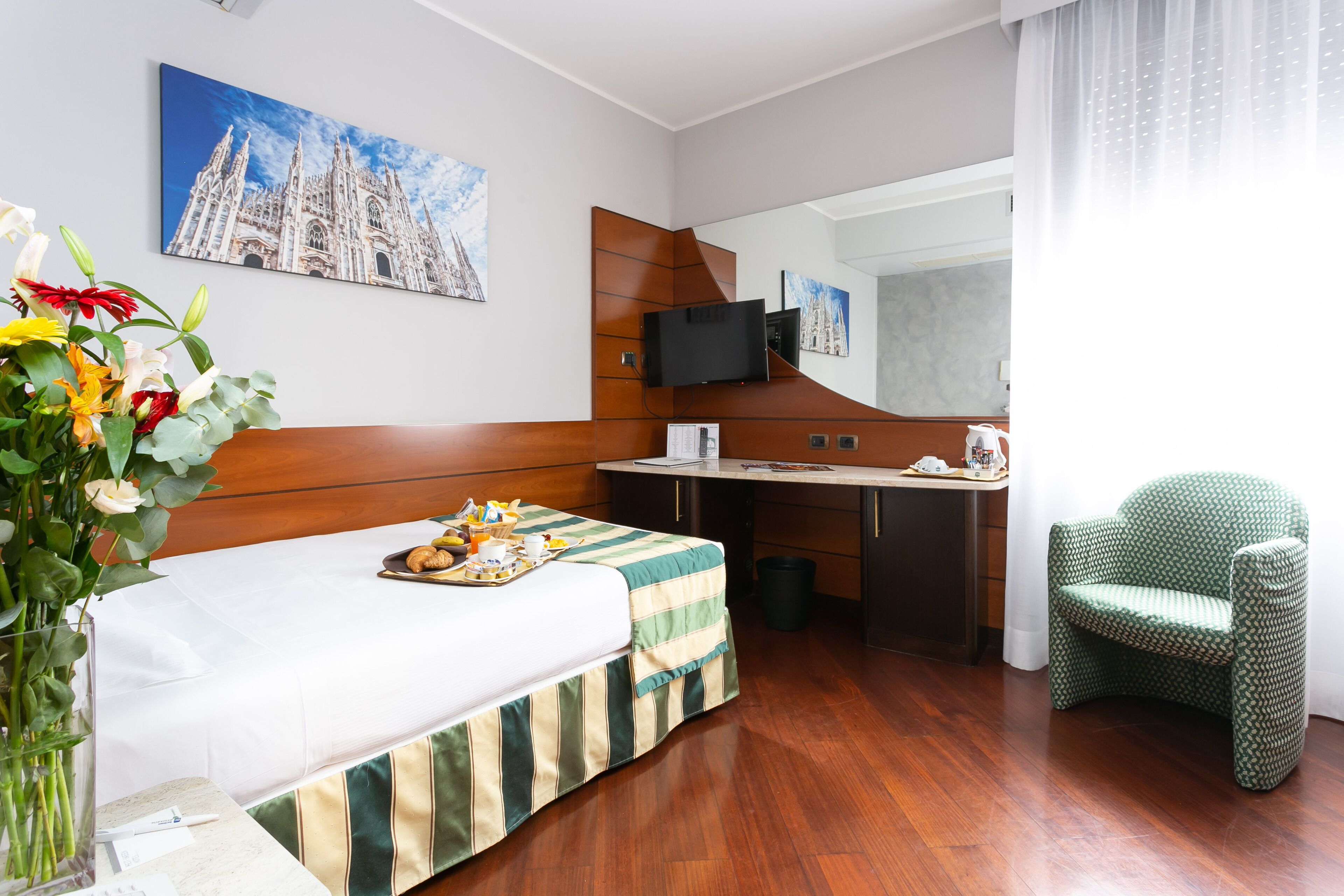 A hotel room with a bed, a desk, a chair, a TV, and artwork on the walls.