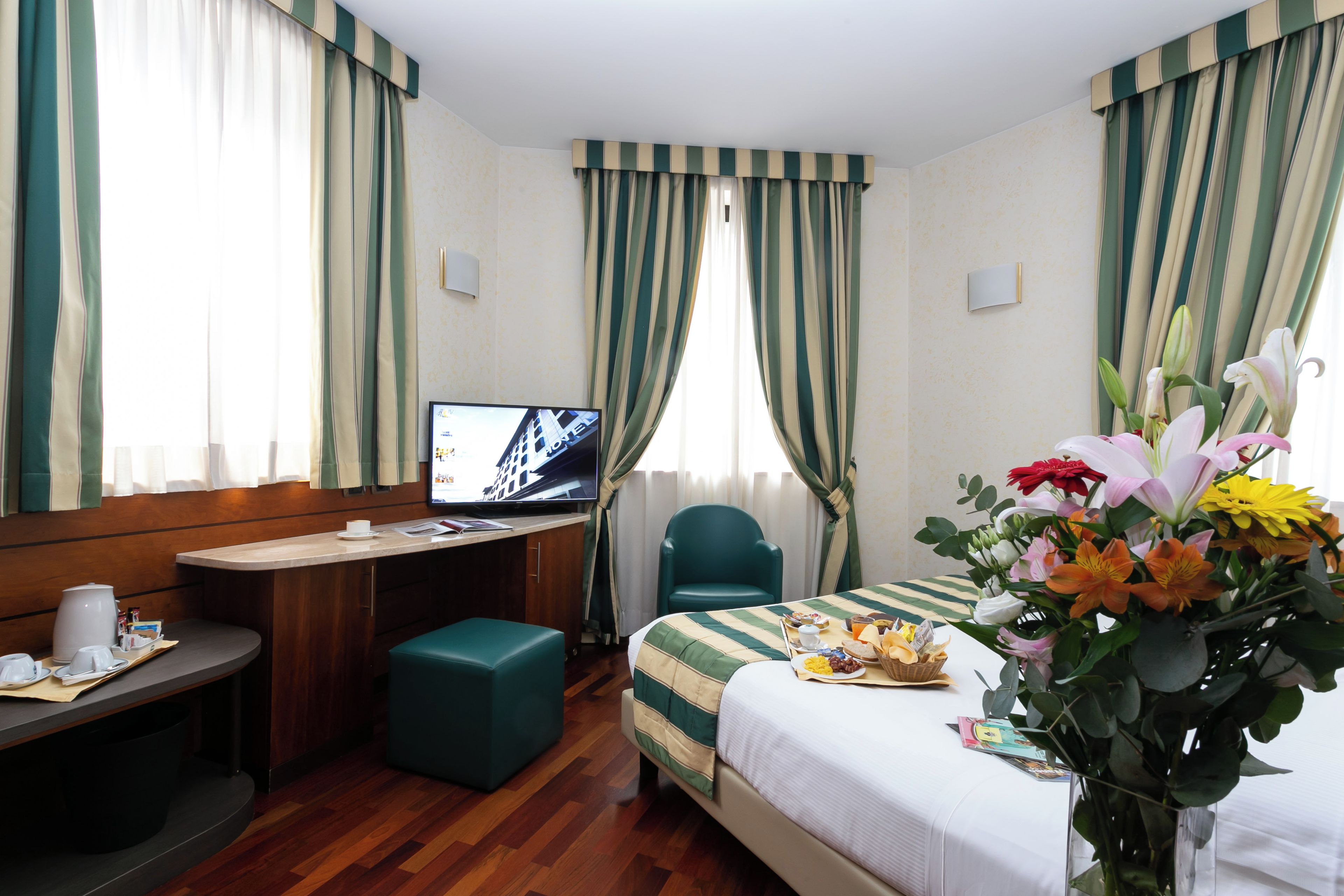 Una camera d'albergo con un letto, una scrivania, una televisione e un tavolo da pranzo apparecchiato per la colazione.