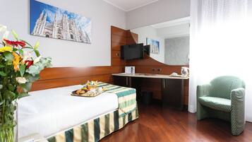 A hotel room with a bed, a desk, a chair, a TV, and a painting of a cathedral.