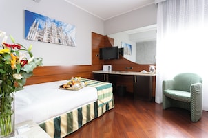 Een hotelkamer met een bed, een bureau, een stoel, een televisie en een schilderij van een kathedraal.