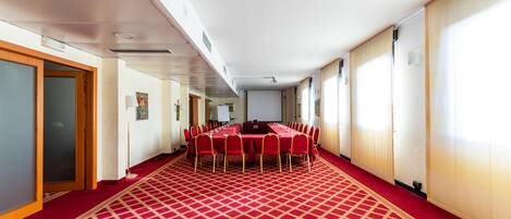 A conference room with a red carpet, a long table with chairs, and a projector screen.