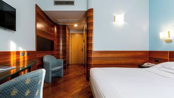 Habitación de hotel con una cama, un escritorio con televisor de pantalla plana, una silla y teléfono instalado en la pared.