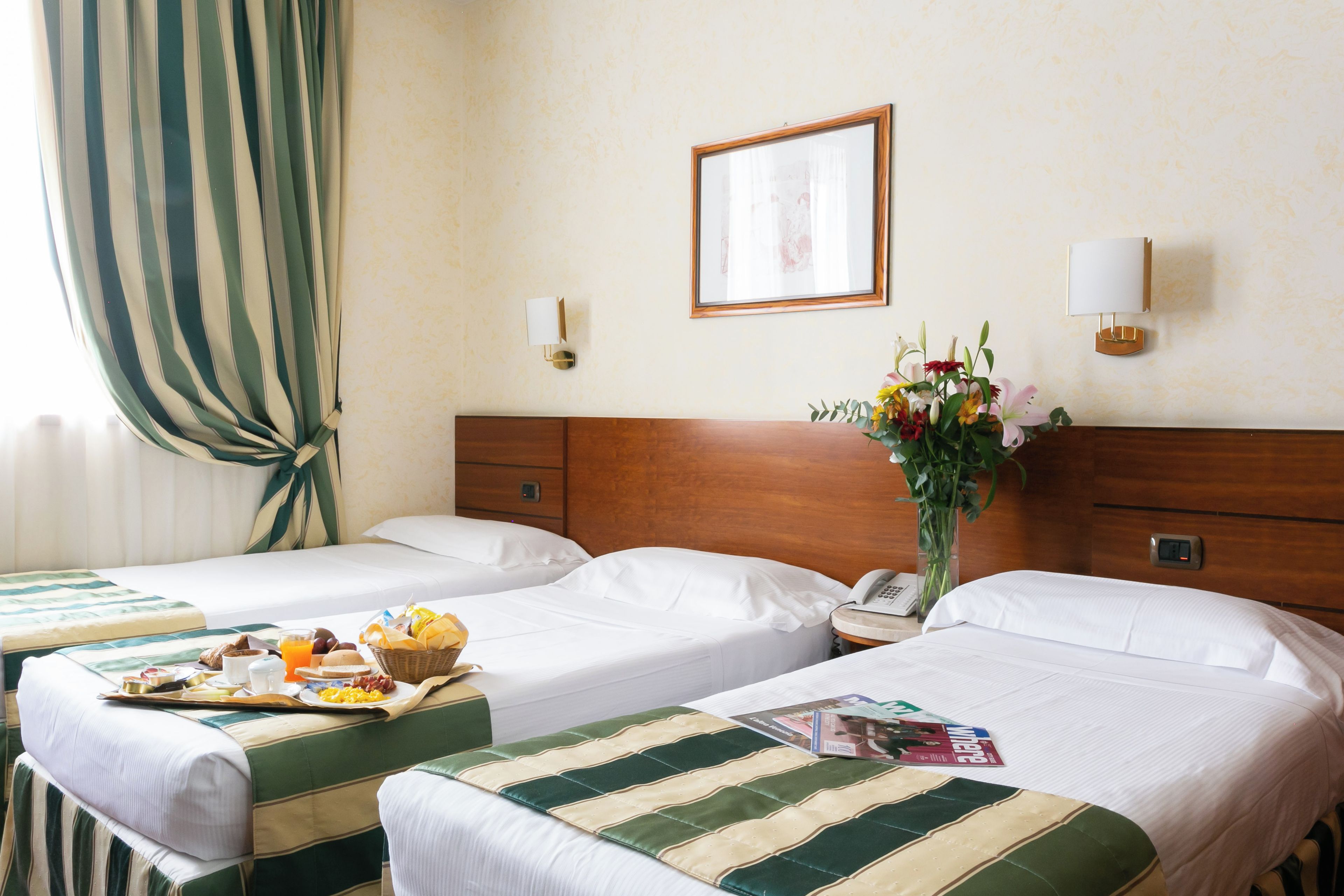 Ein Hotelzimmer mit zwei Betten, einem Frühstücksbrett, einer Blumenvase und einem gerahmten Bild an der Wand.