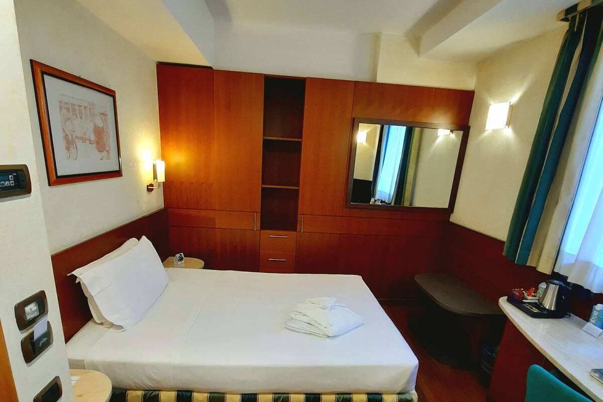Een hotelkamer met een bed, een bureau, een stoel, een spiegel, een ingelijst schilderij en een klein tafeltje.