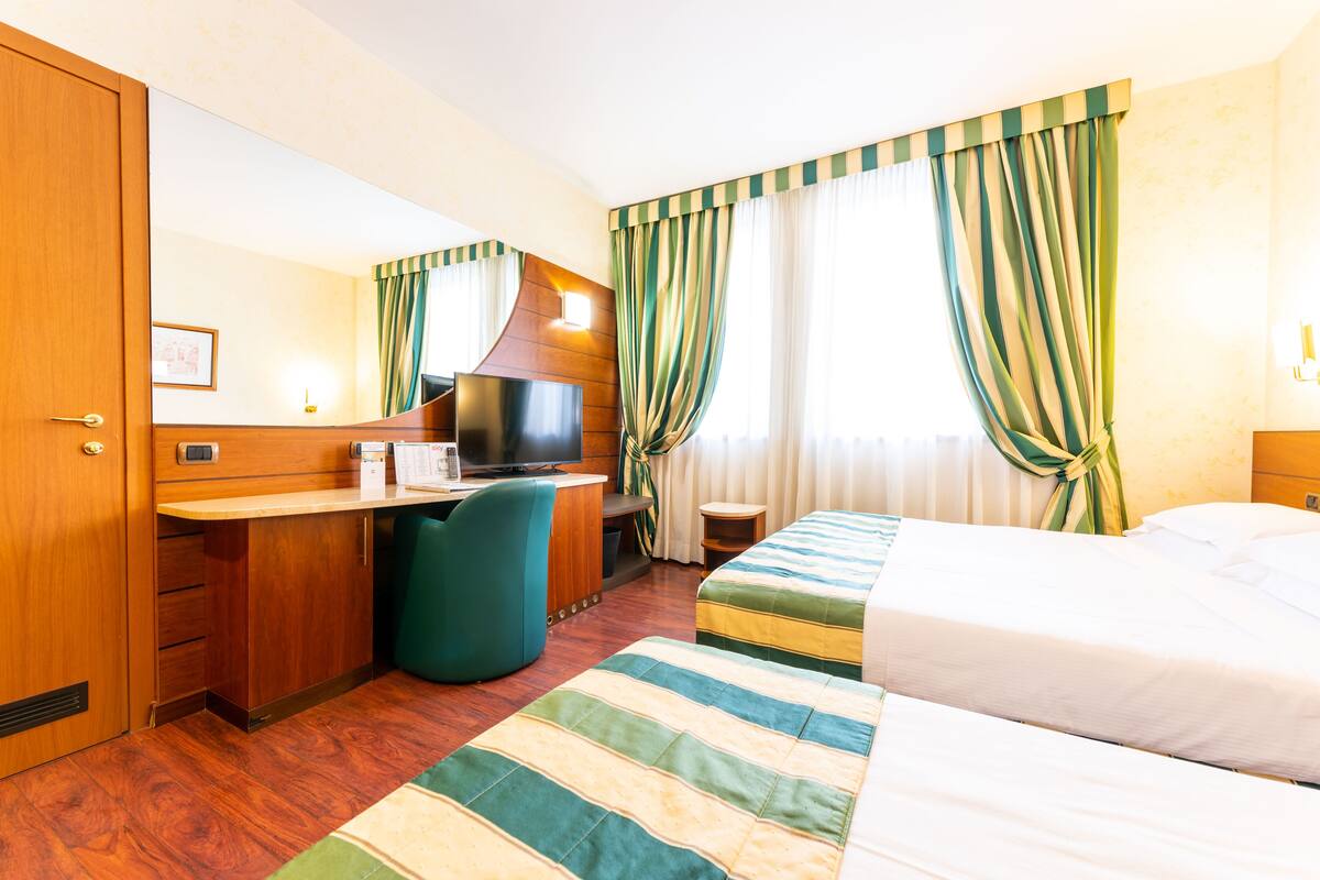 Een hotelkamer met een houten bureau, een televisie, een bed en een raam met gordijnen.