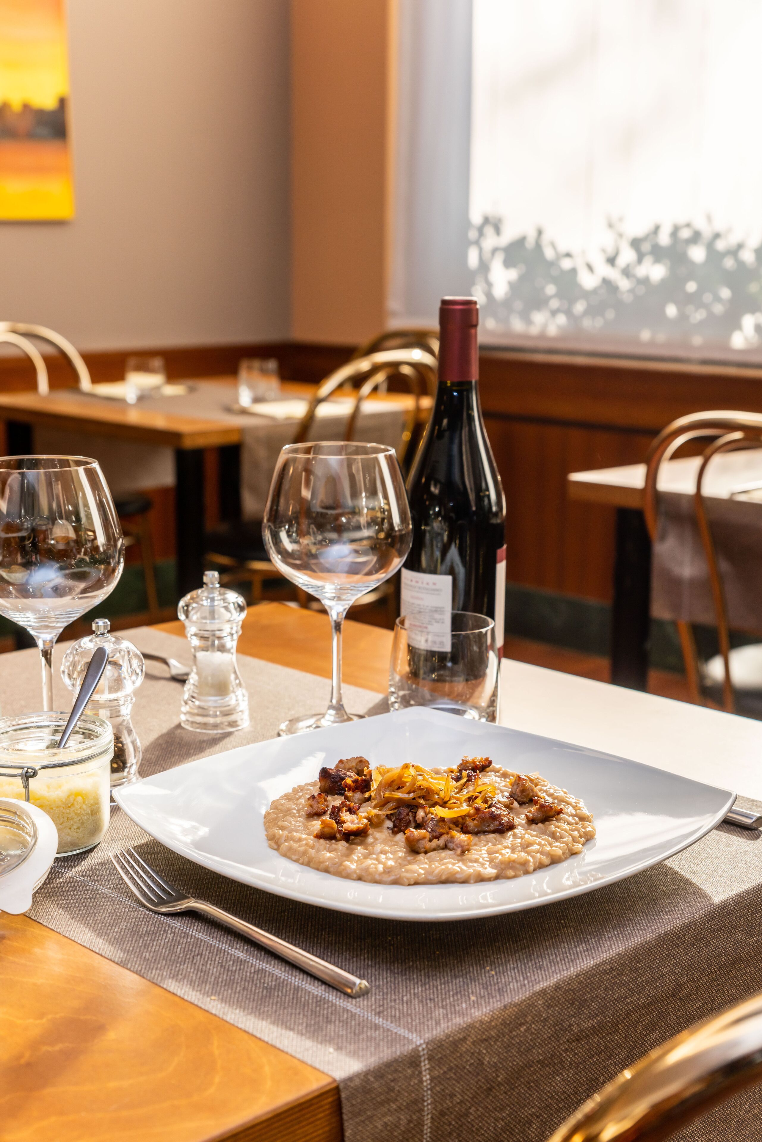 A dining table with a plate of food, wine glasses, and a bottle of wine.