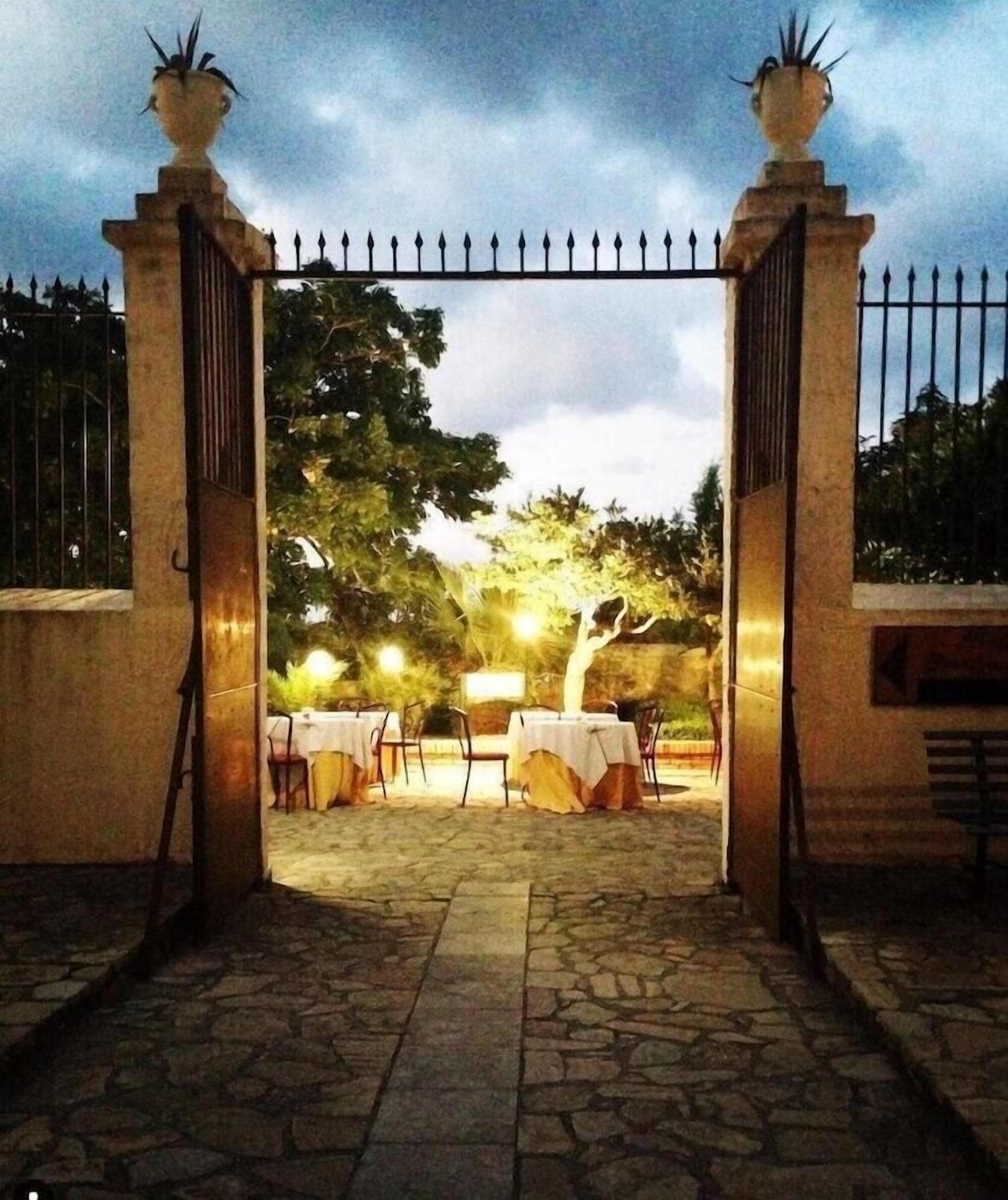 An outdoor dining area with tables and chairs, a stone pathway, and a gated entrance.