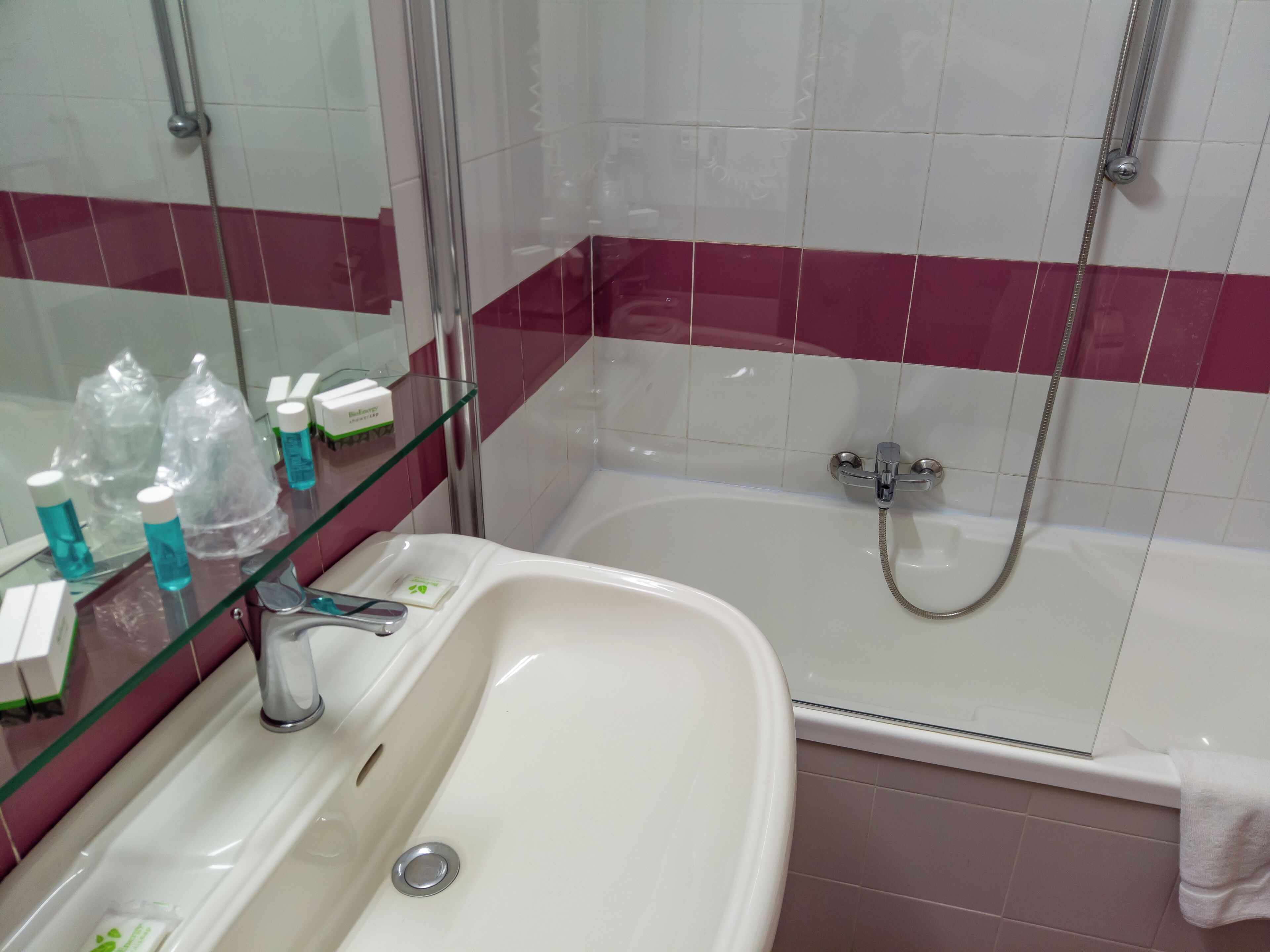A bathroom with a white sink, a glass shelf with toiletries, a mirror, and a shower area.