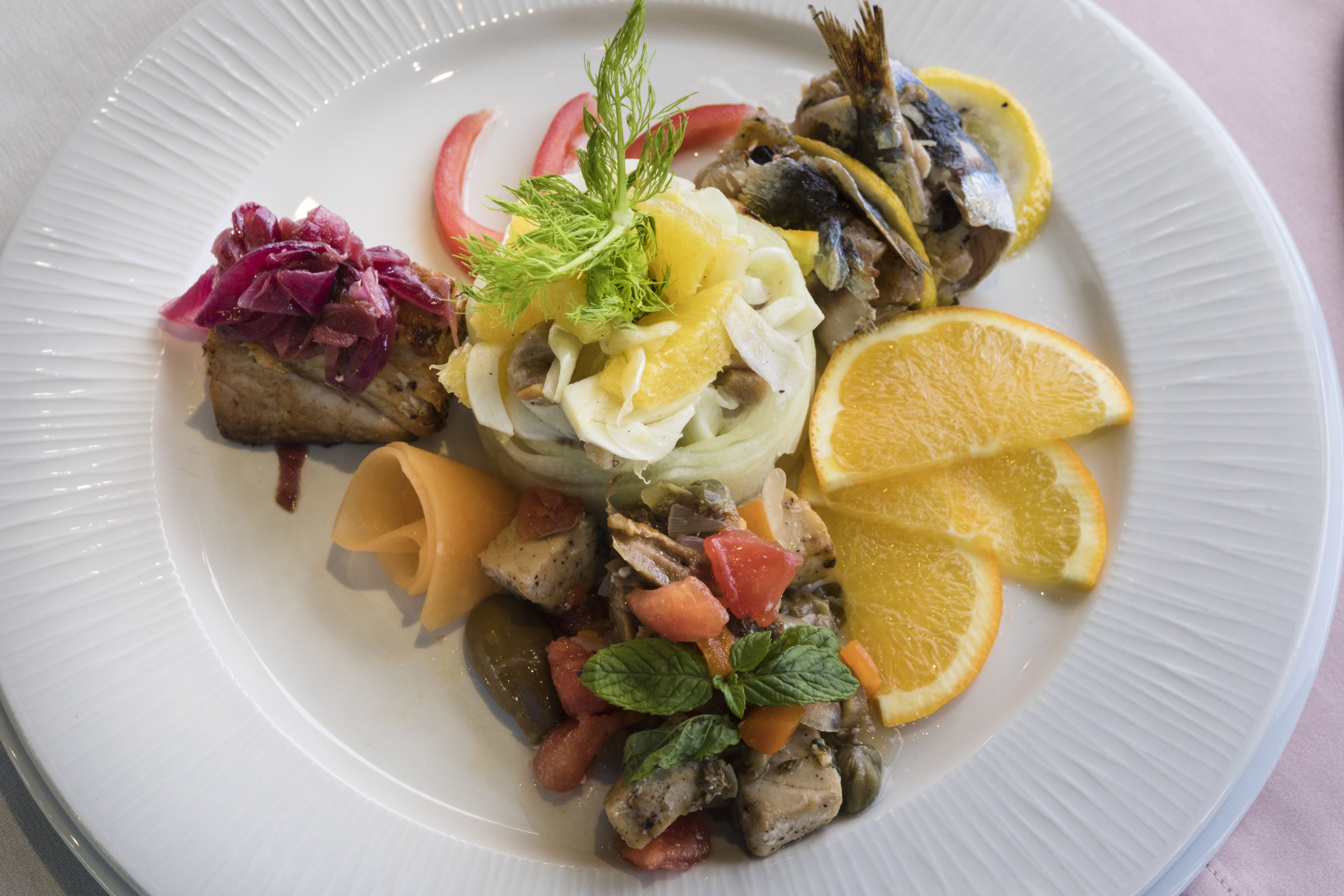 A plate of food with various ingredients including fish, vegetables, and garnishes.