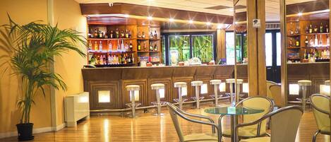 A bar area with wooden flooring, metal bar stools, and a variety of liquor bottles.