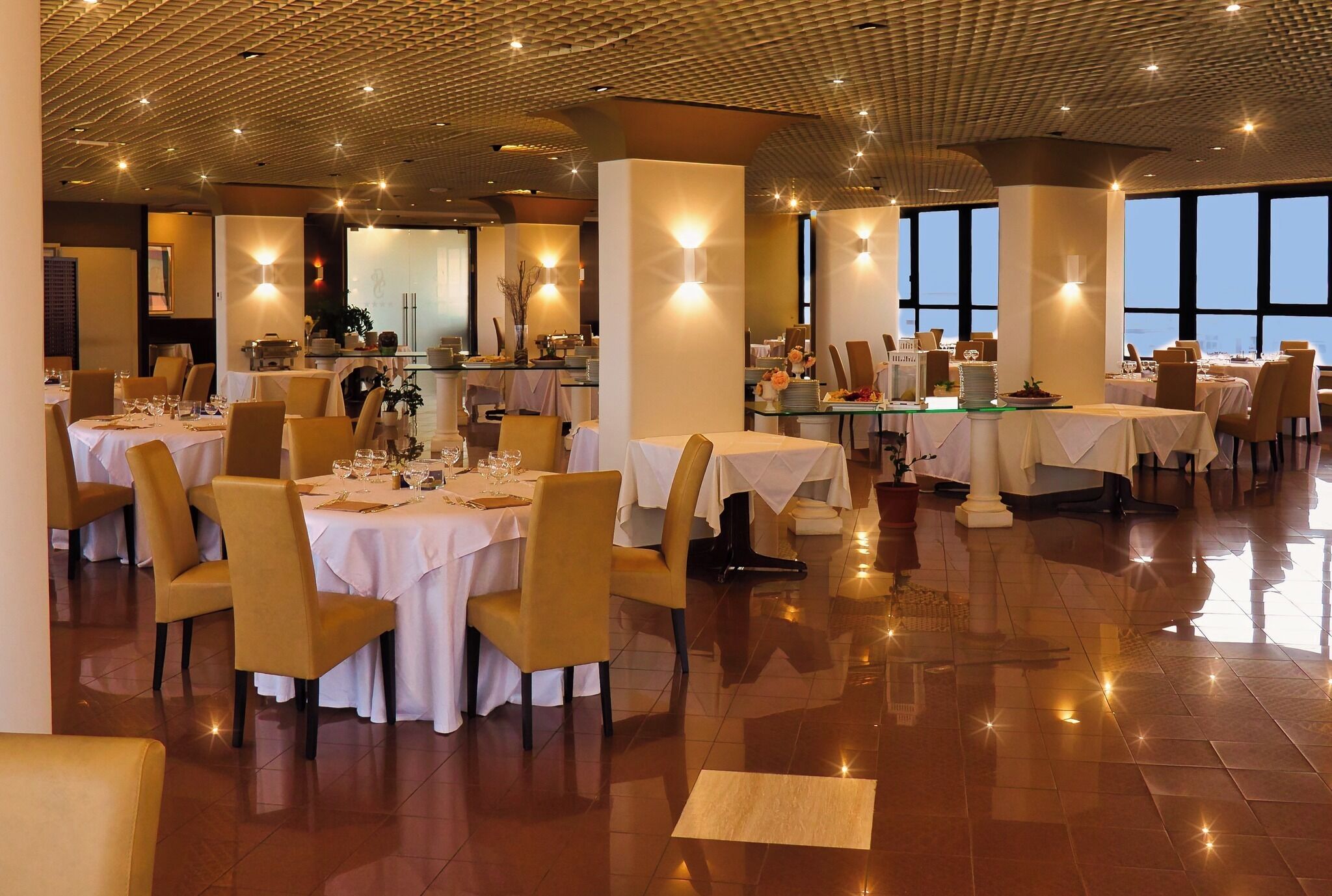 Un comedor amplio con múltiples mesas y sillas, ventanas grandes y un piso pulido.