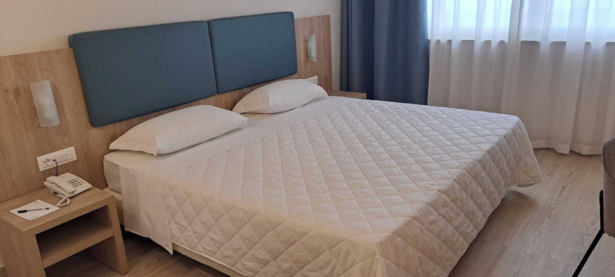 Una cama bien tendida con colcha acolchada, una mesita de noche con teléfono y un aplique de pared.