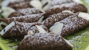 Un piatto di cannoli ricoperti di zucchero a velo e ripieni di crema bianca.