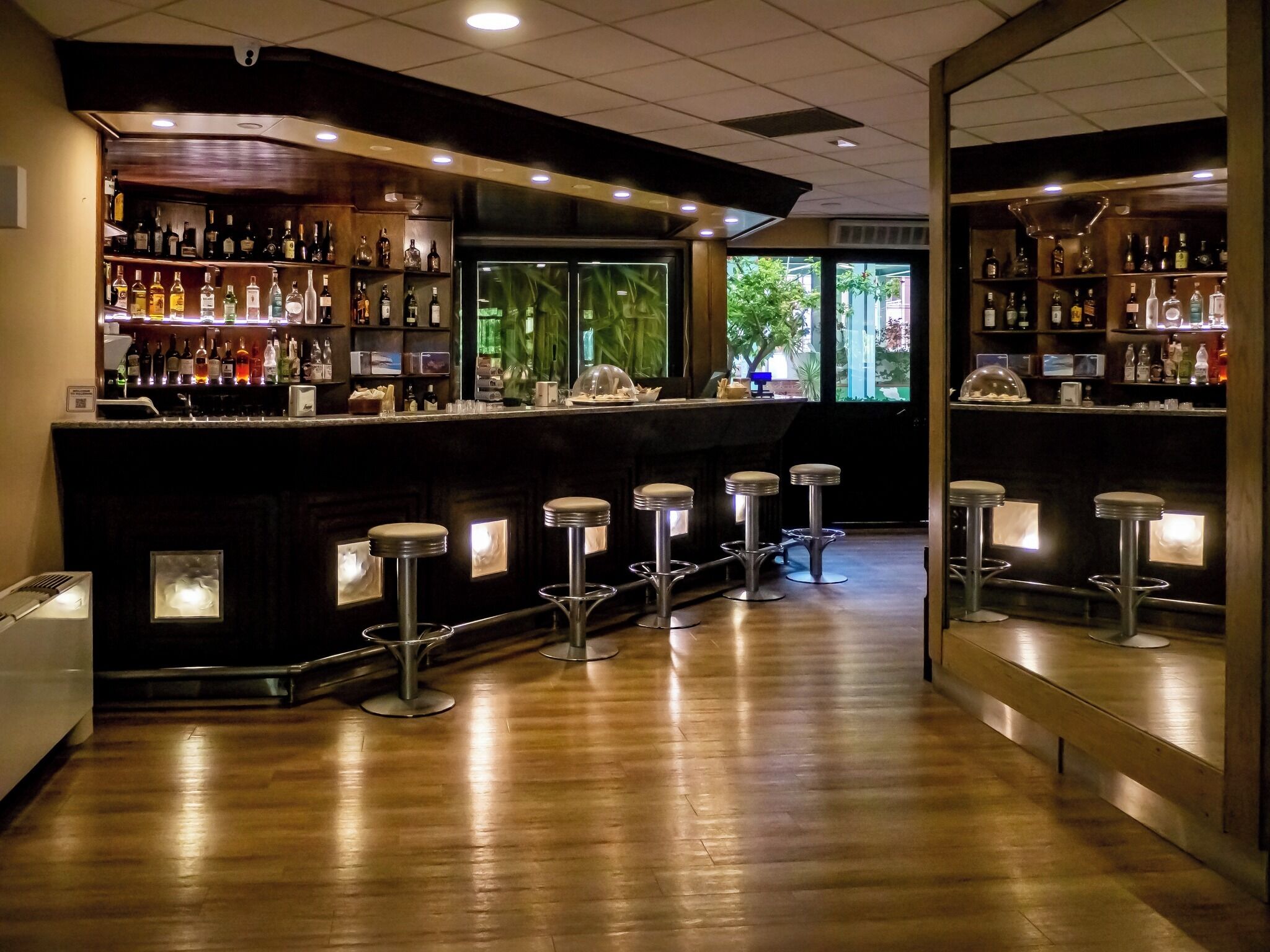 Una zona de bar con suelo de madera, varios taburetes y estantes llenos de botellas.