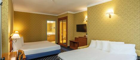 Habitación de hotel con dos camas, un escritorio, una silla, televisión y baño visible a través de una puerta abierta.