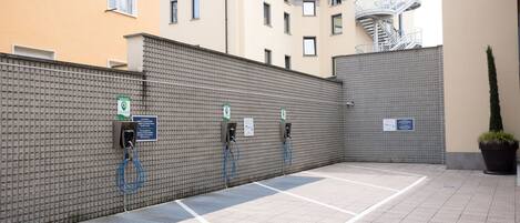 A parking area with electric vehicle charging stations, a brick wall, and a potted plant.
