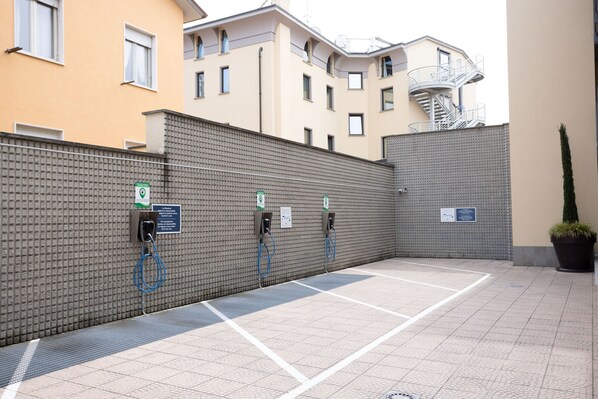 Un área de estacionamiento con estaciones de carga para vehículos eléctricos, un muro de ladrillo y una planta en maceta.