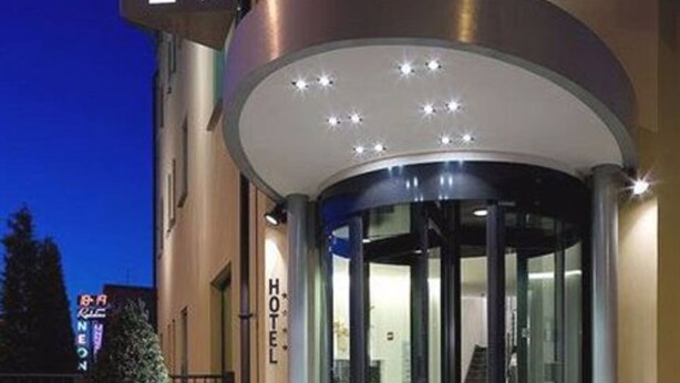 L’entrée d’un hôtel, avec une porte tournante, un escalier menant à l’intérieur et un pot de fleurs au premier plan.