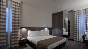Une chambre d’hôtel avec un grand lit, une table de chevet avec un téléphone, un miroir et des rideaux à rayures.