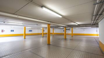 Un vaste parking souterrain avec des piliers jaunes, des murs blancs et un sol carrelé.