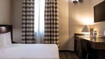 Una habitación de hotel con una cama grande, un escritorio con una silla, un televisor de pantalla plana y una ventana con cortinas a rayas.