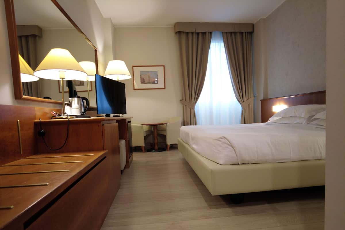 A hotel room with a bed, a desk with a lamp, a television, and a mirror.
